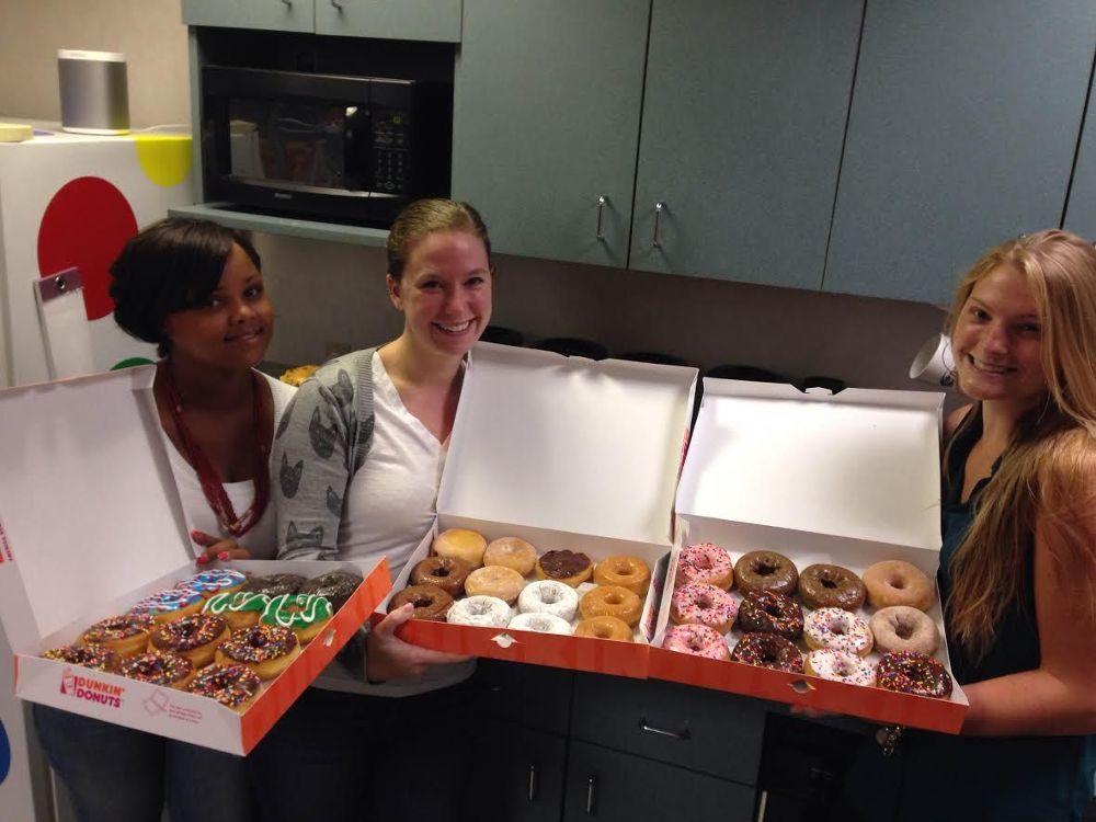 Three people holding boxes of donuts